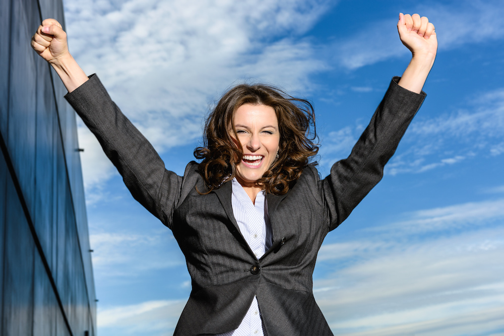 Young Business Woman is jumping for joy in front of blue cloudy sky